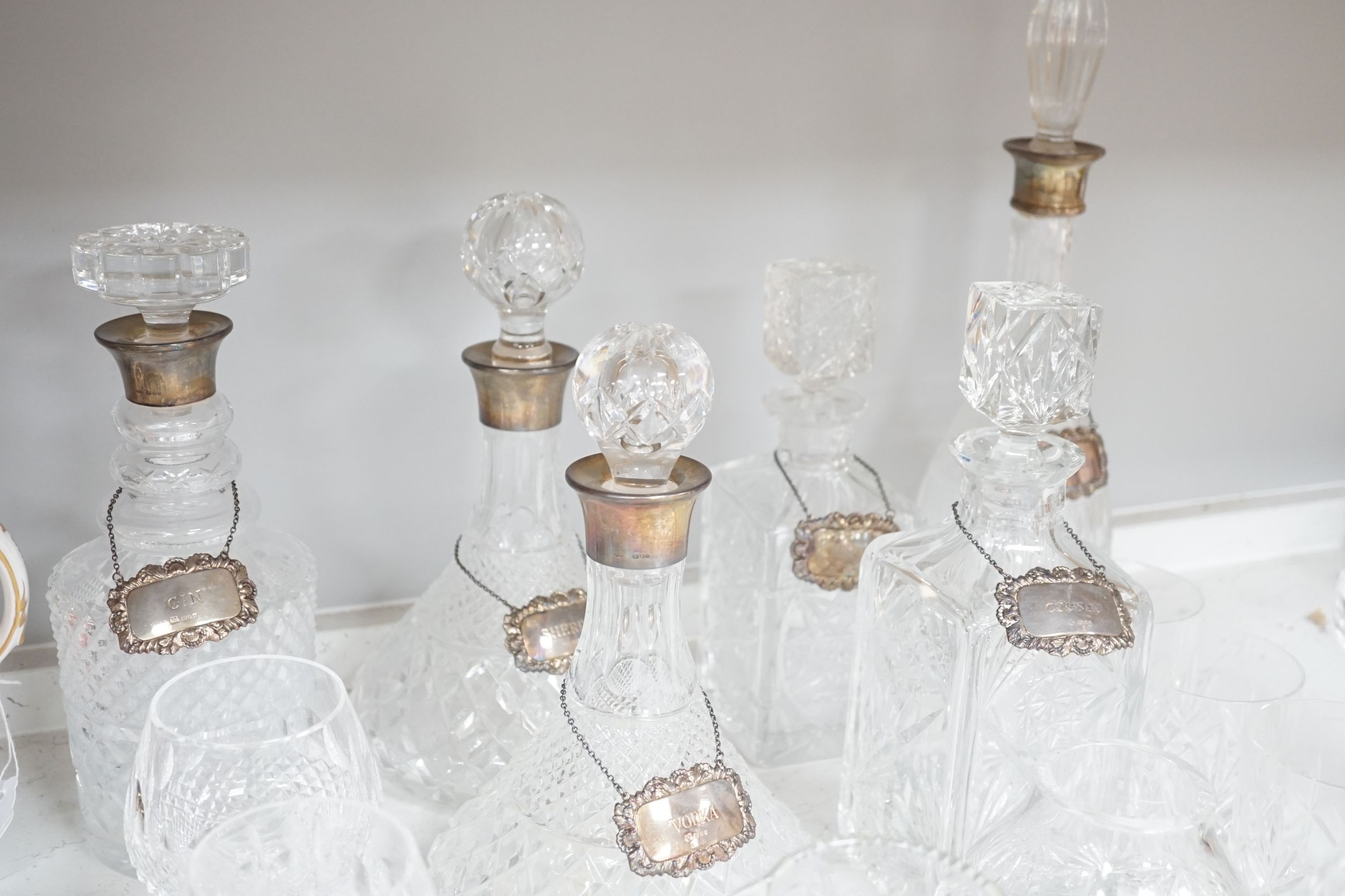 Assorted glassware including six decanters, each with a modern silver wine label